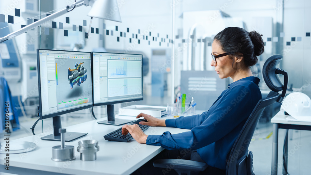 Poster Female Industrial Engineer Solving Problems, Working on a Personal Computer, Two Monitor Screens Show CAD Software with 3D Prototype of Zero-Emissions Engine Being Tested. Working Modern Factory