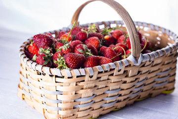 Fototapeta na wymiar Сlose-up shot of ripe strawberries in little basket on white wooden background. 