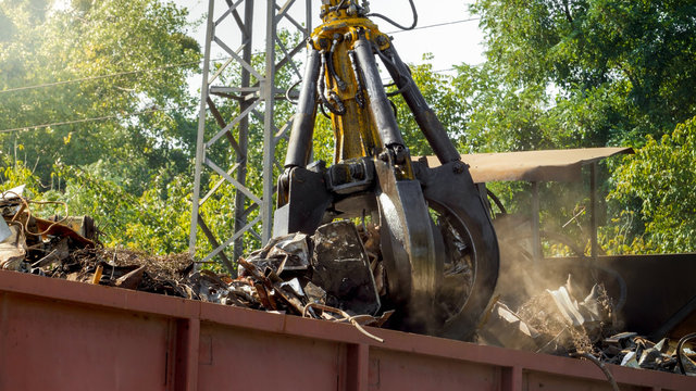Image of metal gripper crushing and destroying old metal pieces on junkyard