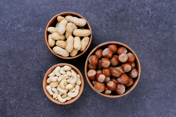 Unpealed hazelnuts, cashews and peanuts in wooden bowls on grey table, top view