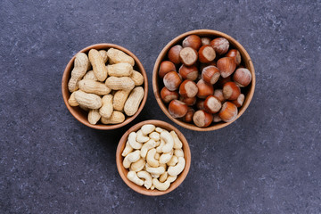 Hazelnuts, cashews and peanuts in wooden bowls on grey table, top view