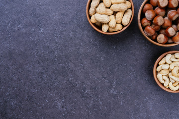 Grey marble background with space for text with hazelnuts, cashews and peanuts in wooden bowls, top view