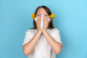 Portrait of a teenage girl with a white scarf who rolls her eyes and sneezes. The concept of seasonal pollen allergy to flowers. The time of spring and summer.