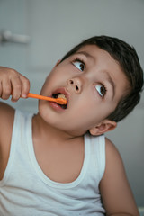 cute kid looking up while brushing teeth in bathroom