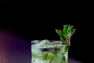 alcoholic cocktail with mint cucumber and liquor in a transparent glass on a dark background with color highlight with bar shots