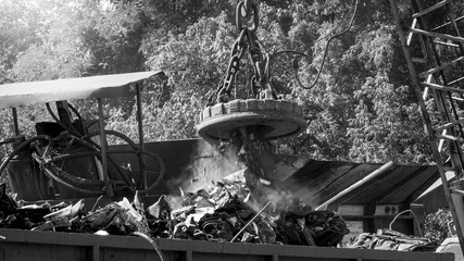 Black and white image of big industrial electric magnet sorting metal scrap on the junkyard