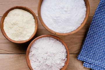 Baking ingredients: rice flour, corn flour and whole grain flour in wooden bowls on oak table with blue napkin. Flat lay top view, studio shot