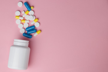 Assorted pharmaceutical medicine pills, tablets and capsules over a pink background