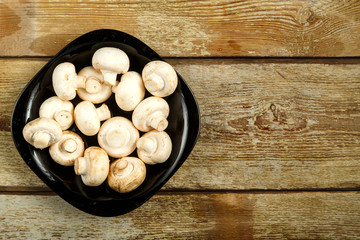 Champignons in a black plate on a table of rough boards.