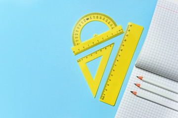 Obraz premium Squared school notebook, pencils and set of rulers on a blue background with copy space