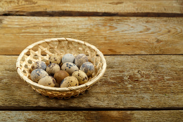 Fresh quail eggs in a wicker basket on a wooden table.