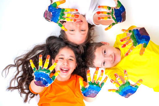 Three happy and smiling children are looking at the camera and holding out their hands in paints. Rainbow on the hands. The concept of a happy childhood and children's day.