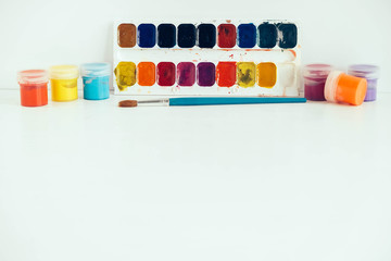 Colorful gouache paints and brush for painting on white wooden table. Copy, empty space for text