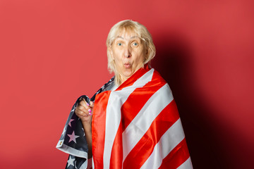 Old woman holds US flag on pink background. Concept patriot, holiday, independence day, memorial day, US visa, emigration to the USA