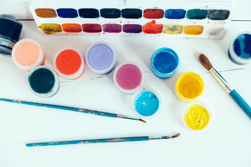 Colorful gouache paints and brushes for painting on white wooden table. Top view. Copy, empty space...