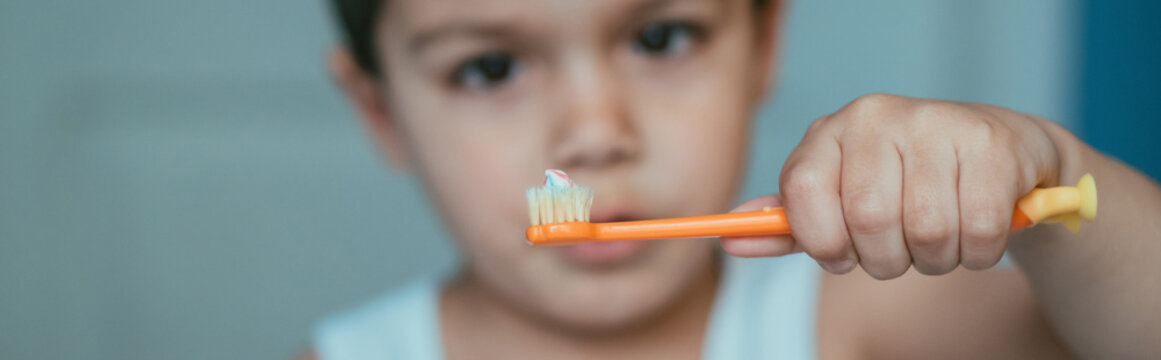 selective focus of cute boy looking at toothbrush with toothpaste, horizontal image
