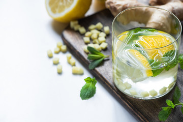selective focus of fresh ginger lemonade in glass with lemon and mint on wooden board on white background