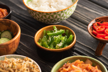 selective focus of sesame on green bell peppers near rice and korean side dishes on wooden surface