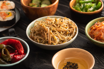 selective focus of mung beans near pickled chili peppers, sesame in oil and side dishes on wooden surface