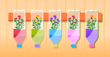 Multi-colored flowers in bottles hang on a wooden plank on the wall. Reuse plastic bottle as flower pots in home garden and craft recycle theme. Growing decorative flower in a plastic bottle for water