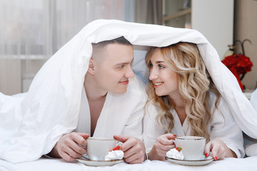 Couple under the covers with a cup of coffee in bed.