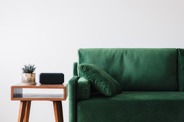 close up view of green sofa with pillow and wooden coffee table with plant and alarm clock