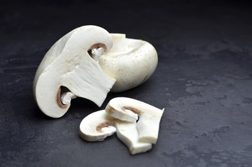 Fototapeta premium Raw champignon mushrooms, cutted and whole one, dark grey slate background. Vegitarian food cooking. Copy space.