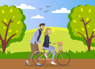 Happy young man is helping a smiling woman to ride a bicycle on the road at summer forest background. Girl is riding a pink bicycle with a bouquet of flowers in a basket. Romantic ride in the park