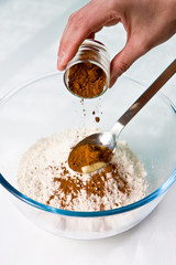 Someone`s hand adding the chocolate powder to the crystal bowl with flour for cooking