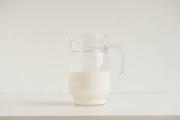 Glass jug with milk on a white table. Copy, empty space for text
