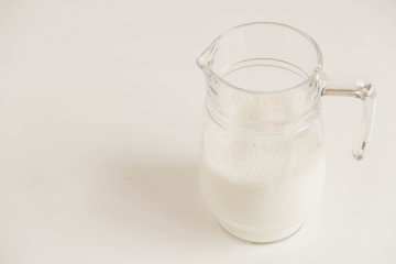 Glass jug with milk on a white table. Copy, empty space for text
