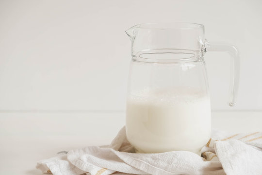 Glass jug with milk and napkin on a white table. Copy, empty space for text