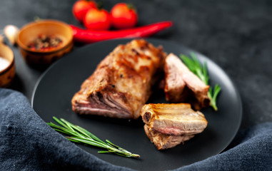 Grilled pork ribs on a black plate with spices on a stone background