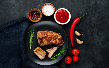 Grilled pork ribs on a black plate with spices on a stone background