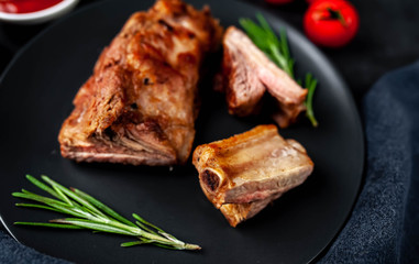 Grilled pork ribs on a black plate with spices on a stone background