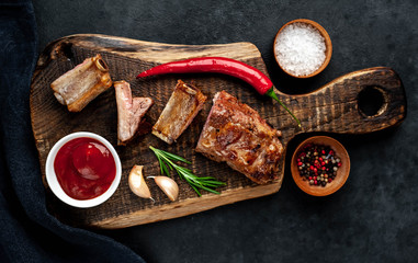 Grilled pork ribs on a cutting board with spices on a stone background