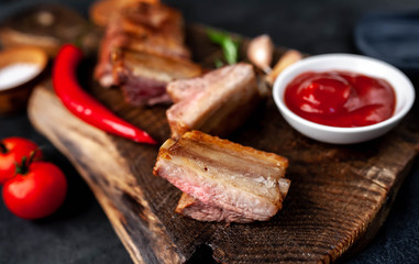 Grilled pork ribs on a cutting board with spices on a stone background