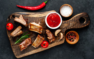 Grilled pork ribs on a cutting board with spices on a stone background