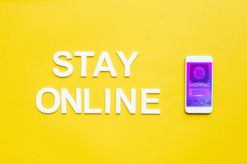 Top view of stay online lettering and smartphone with online shopping app on yellow surface