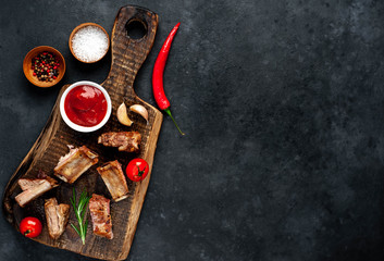 Grilled pork ribs on a cutting board with spices on a stone background