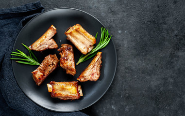 Grilled pork ribs on a black plate with spices on a stone background
with copy space for your text
