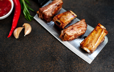 Grilled pork ribs over meat knife with spices on a stone background with copy space for your text
