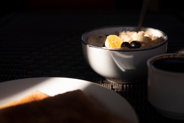 Oatmeal with bananas and berries in the morning light. Coffee, breakfast.