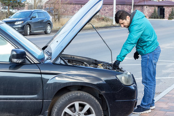 A bearded man standing next to the open hood of a black car during the repair process. Oil or antifreeze filling, machine self service and diagnostic