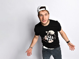 Fototapeta na wymiar Hipster man in cap, black t-shirt with print, bracelets, jeans and sneakers. He is smiling, posing isolated on white. Full length