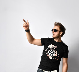 Hipster fellow in sunglasses, black t-shirt with print, bracelets. He is pointing at someone,...