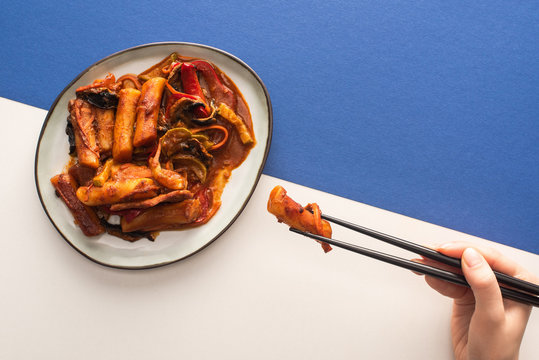 top view of woman holding chopsticks with korean topokki on white and blue