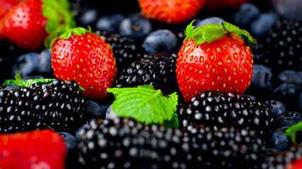 Closeup photo of mint leaves lying big heap of fresh tasty berries on table