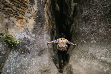 A young hipster man with a backpack and in an orange jacket enters a mountain cave. Travel concept