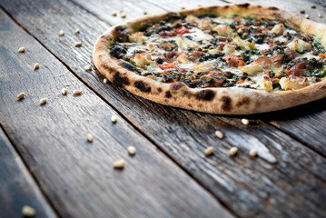 A close up of a vegan styled pizza on a wooden table with a nice arrangements of the pine nuts...